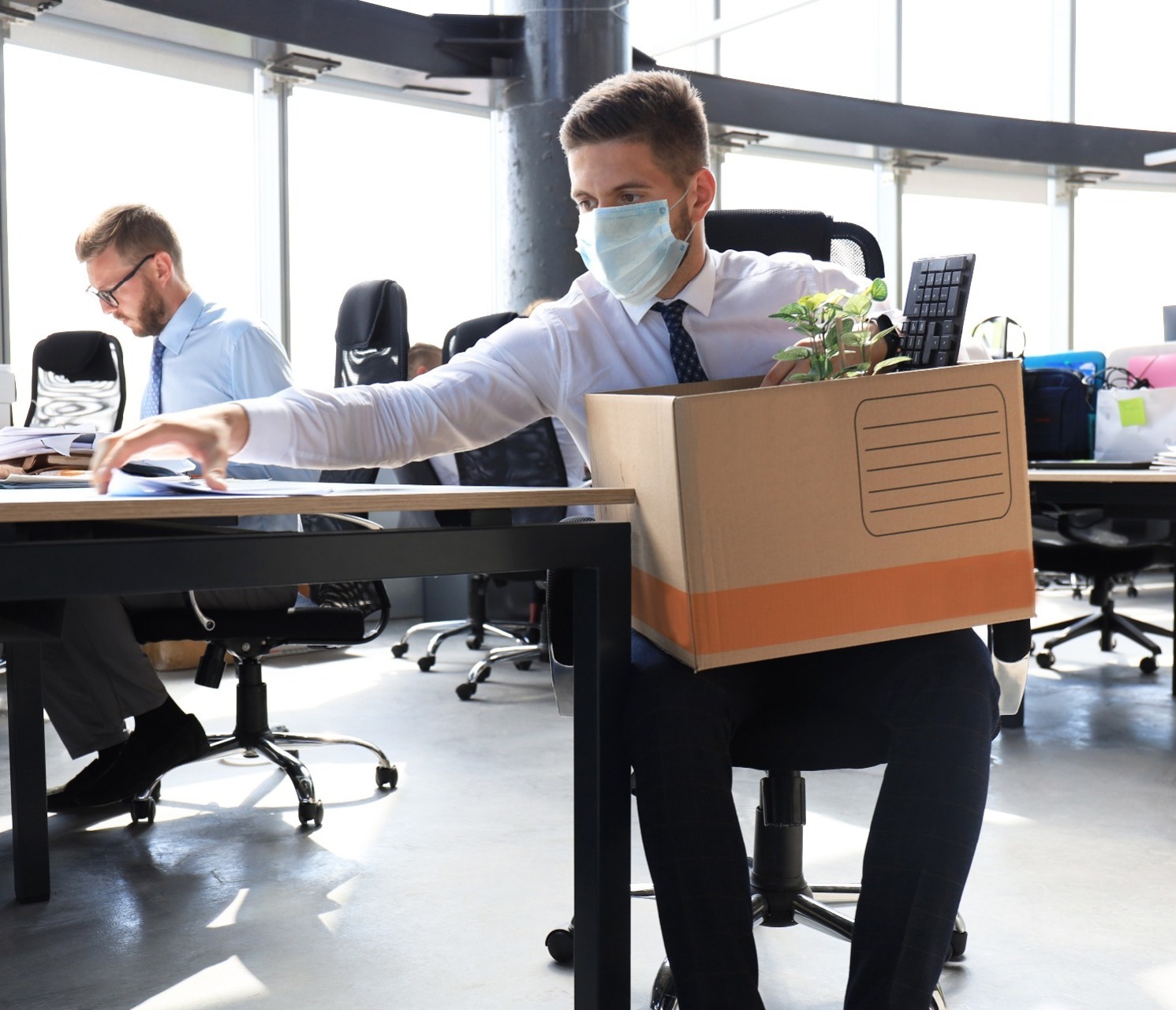 Man wearing a mask clearing his desk after being dismissed