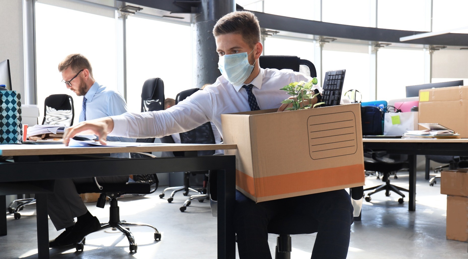 Man wearing a face mask emptying his desk contents into a cardboard box